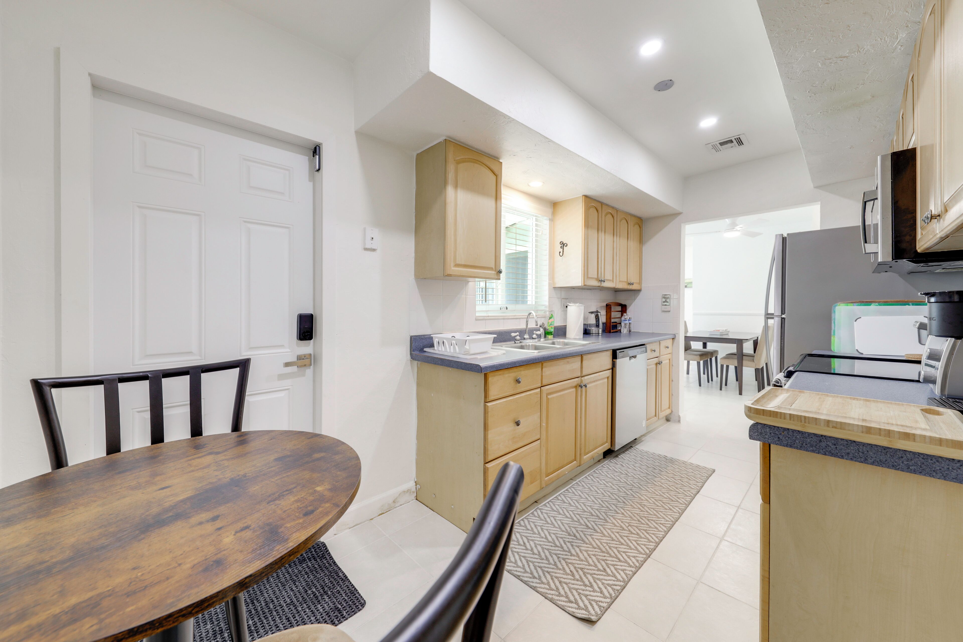 A modern kitchen with wooden cabinets, a dining table, chairs, and a refrigerator.