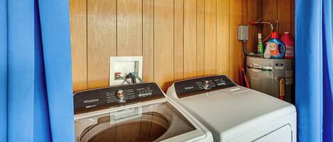 A laundry room with two washers and dryers, wooden walls, a power outlet, and a water heater.