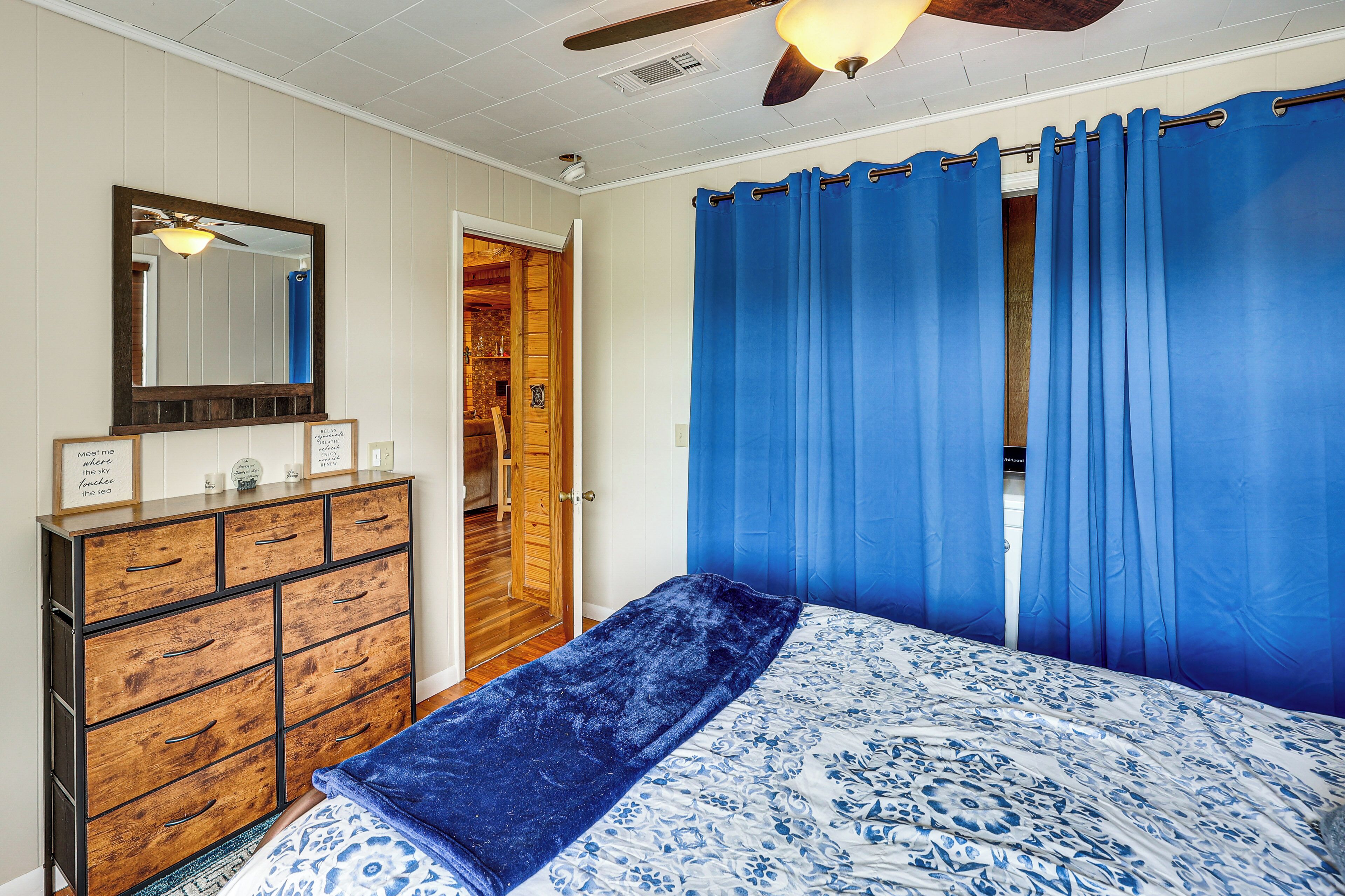 Ein Schlafzimmer mit einem Bett, einer Kommode, einem Spiegel und blauen Vorhängen.