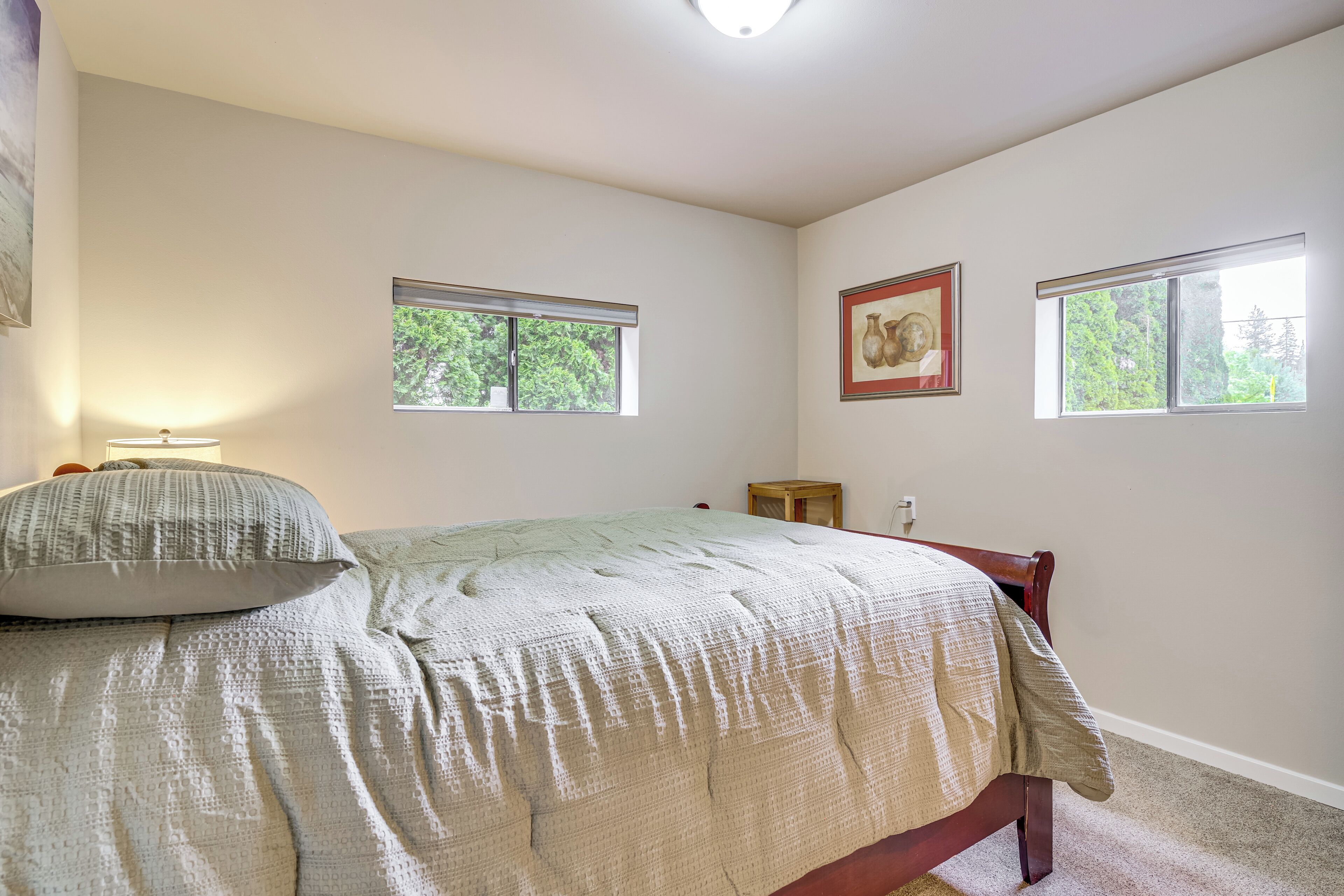 A bedroom with a bed, two windows, a nightstand, and a framed picture on the wall.