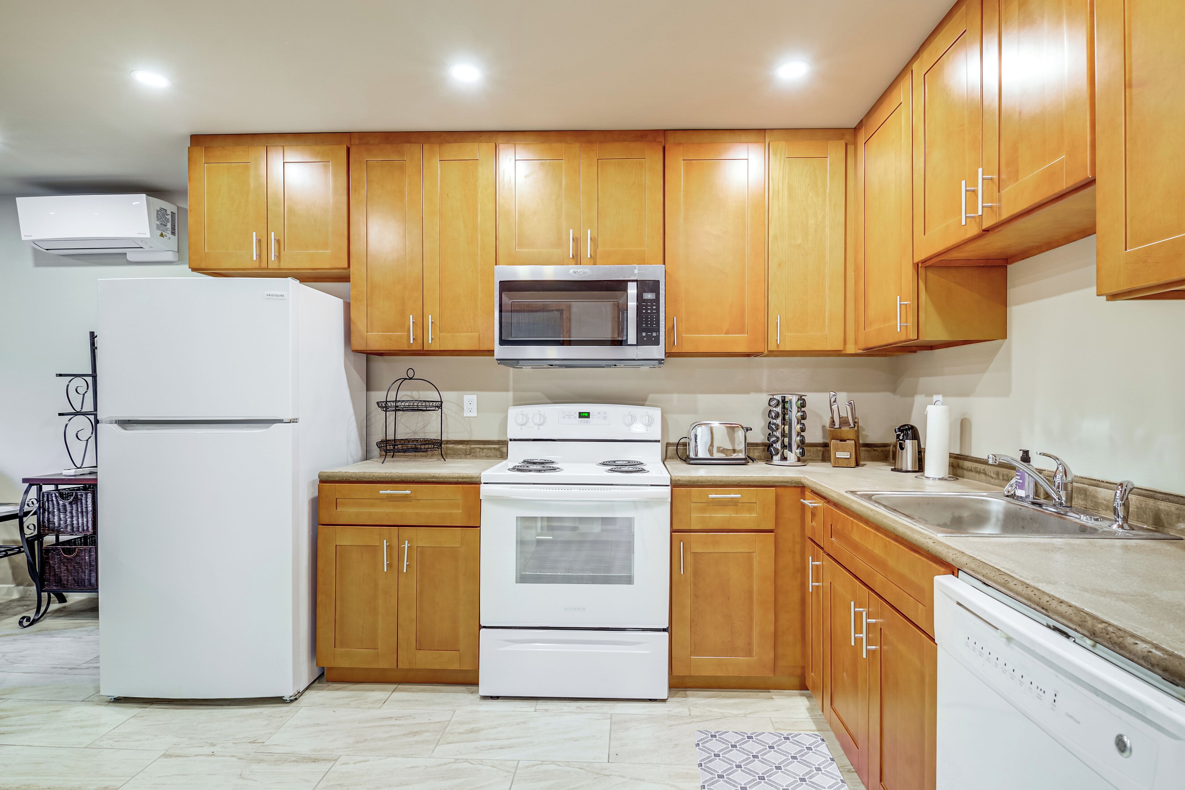 Una cocina con armarios de madera, un microondas de acero inoxidable, un refrigerador blanco, una estufa y un lavavajillas.