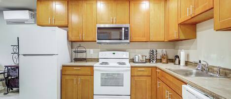 Una cocina con armarios de madera, un microondas de acero inoxidable, un refrigerador blanco, una estufa y un lavavajillas.