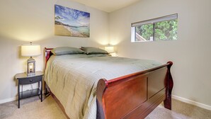 Un dormitorio con cama, mesitas de noche, lámpara, un cuadro y una ventana.