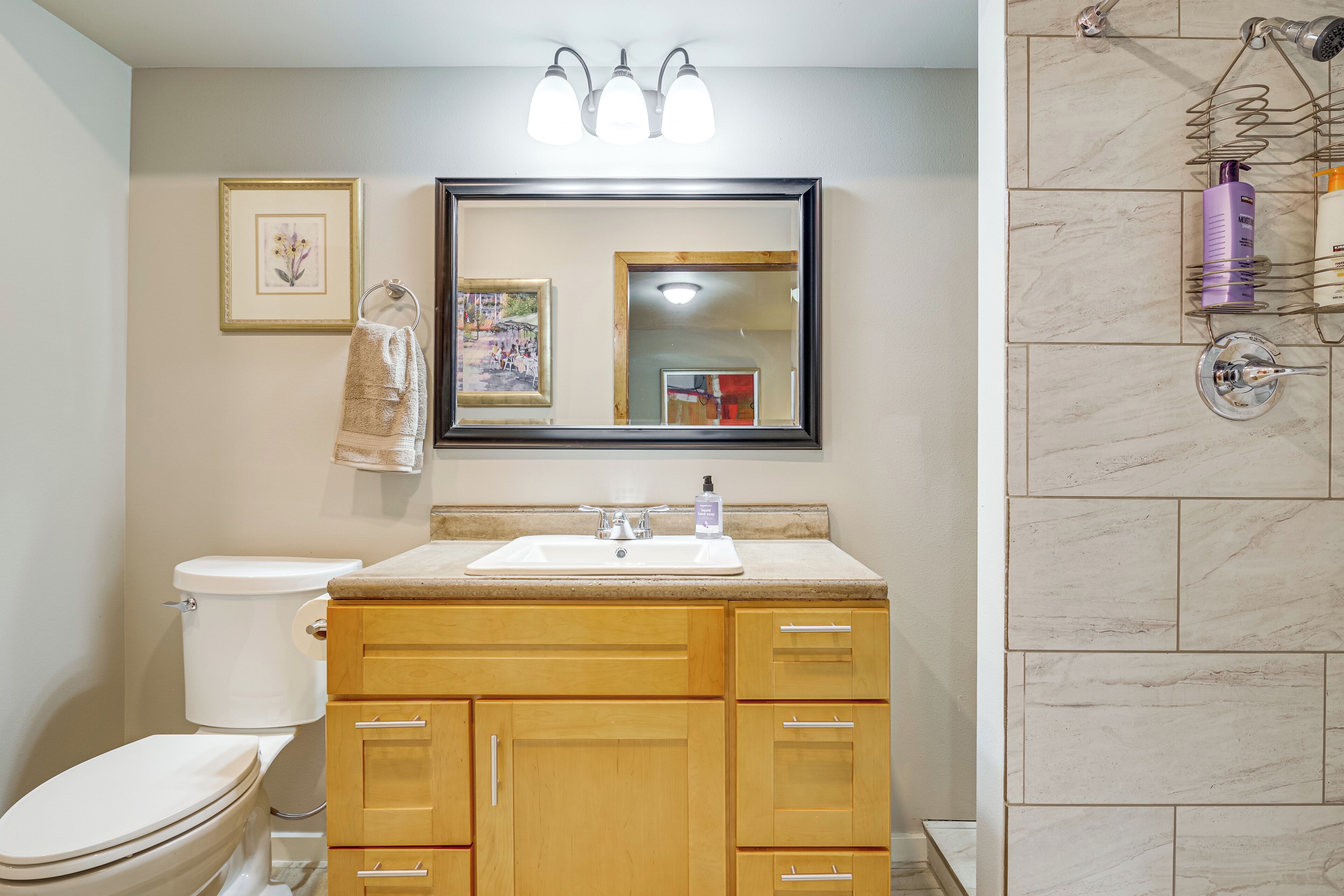 A bathroom with a toilet, sink, wooden cabinets, a mirror, and a shower area.