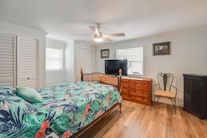 Un dormitorio con cama, televisor, cómoda, silla y ventilador de techo.
