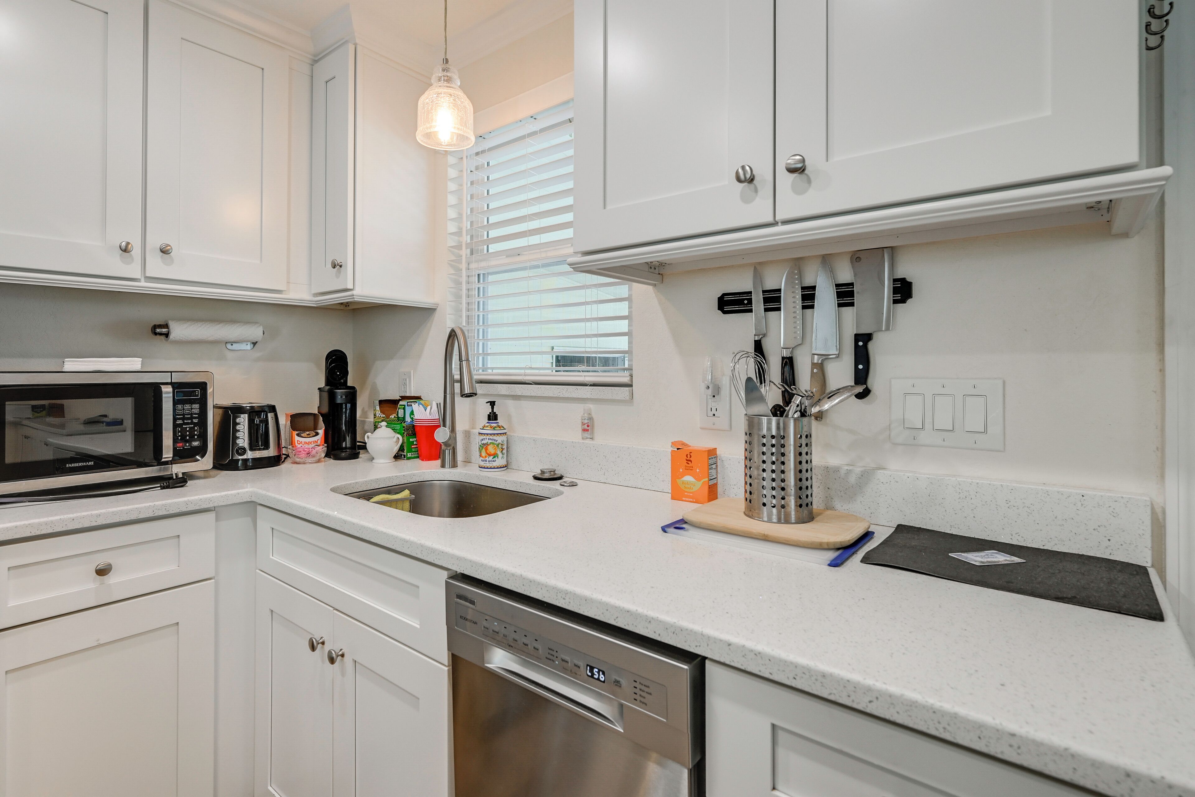 A modern kitchen with white cabinetry, a stainless steel dishwasher, a microwave, and a coffee maker.