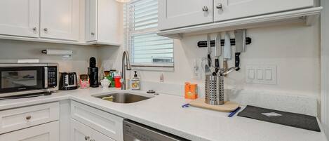 A modern kitchen with white cabinetry, a stainless steel dishwasher, a microwave, and a coffee maker.