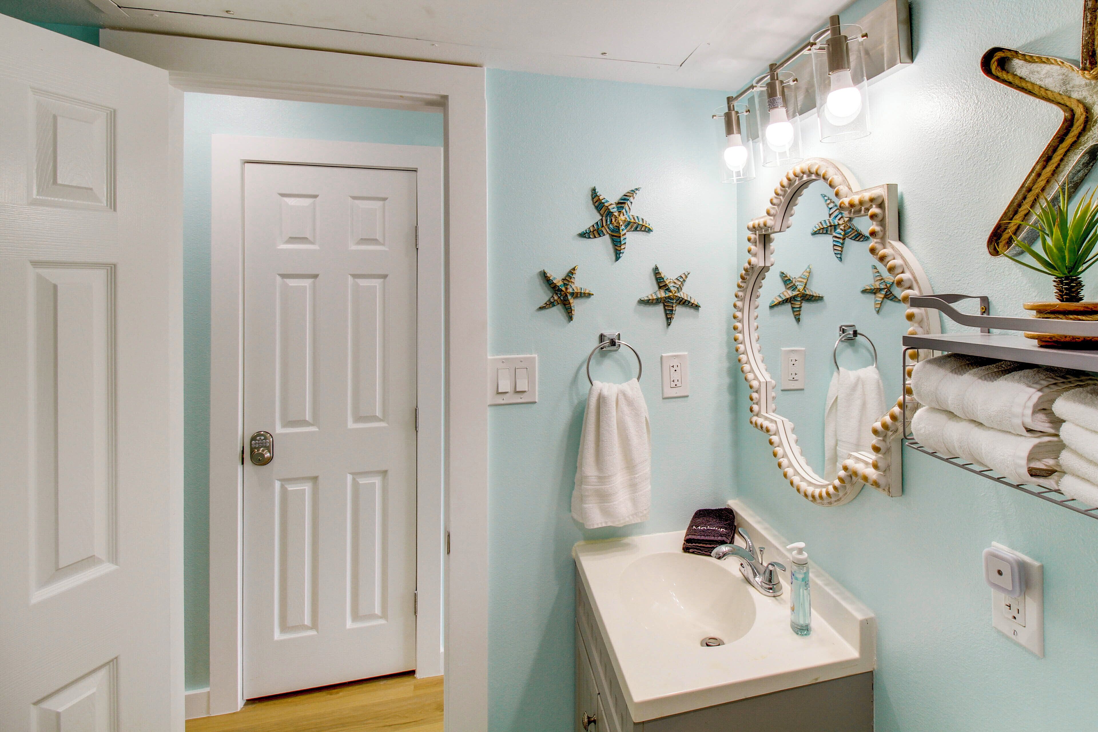 Un baño con un lavamanos blanco, un espejo con decoraciones de estrellas de mar y una puerta.