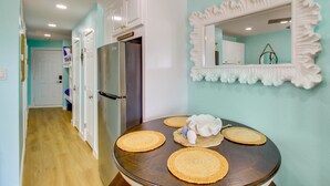 A kitchen with a refrigerator, a dining table with placemats, and a decorative mirror. - Poolside Fun, Ocean Strolls! Corpus Christi Escape (Corpus Christi)