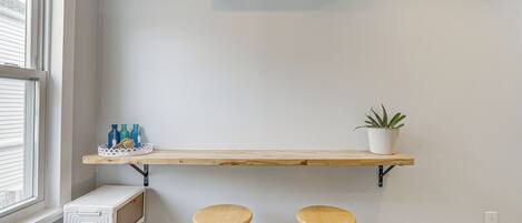 A room with a window, an air conditioner, a shelf with bottles and a plant, and two stools.