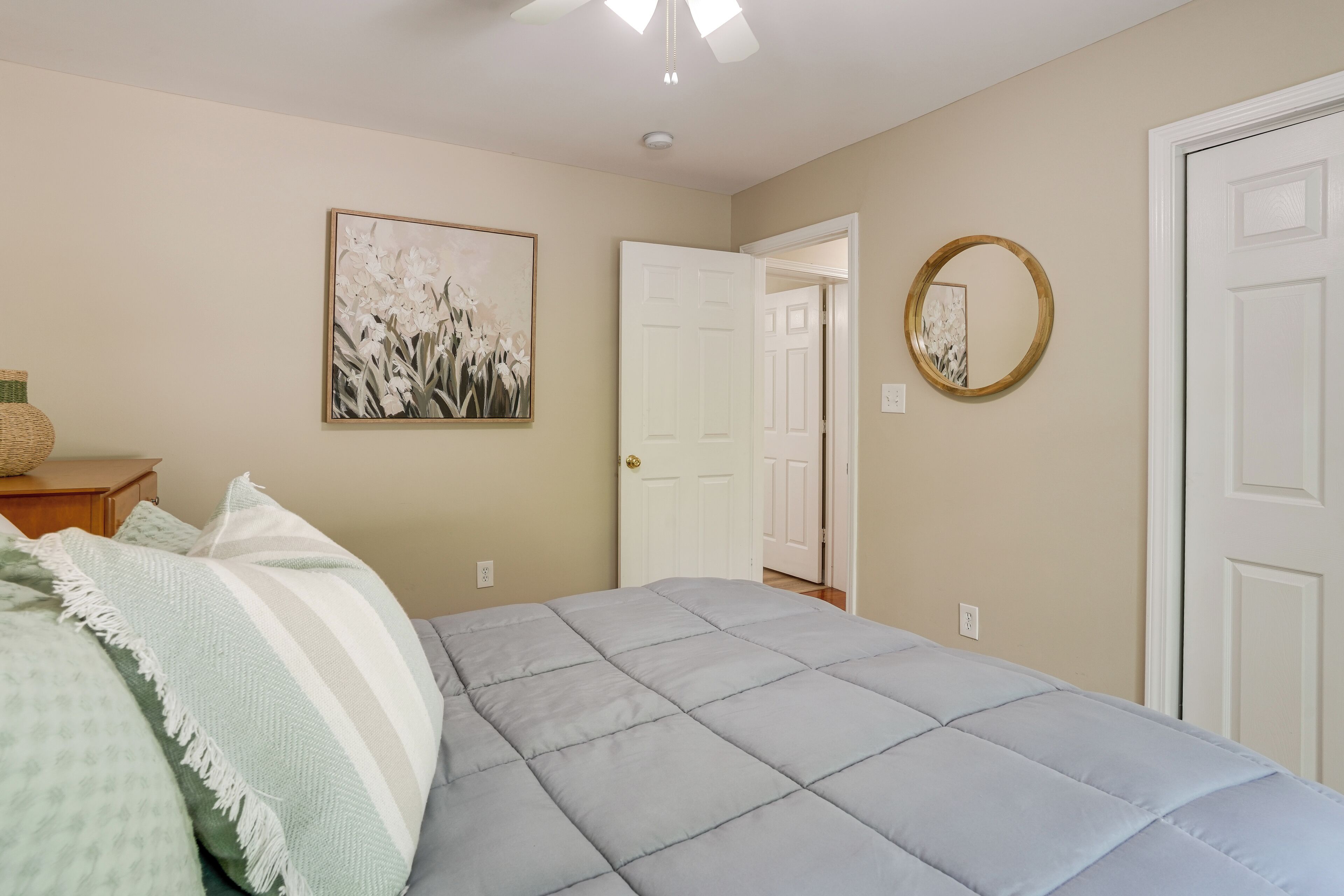 Quarto com cama, porta, espelho fixado na parede e quadro emoldurado.