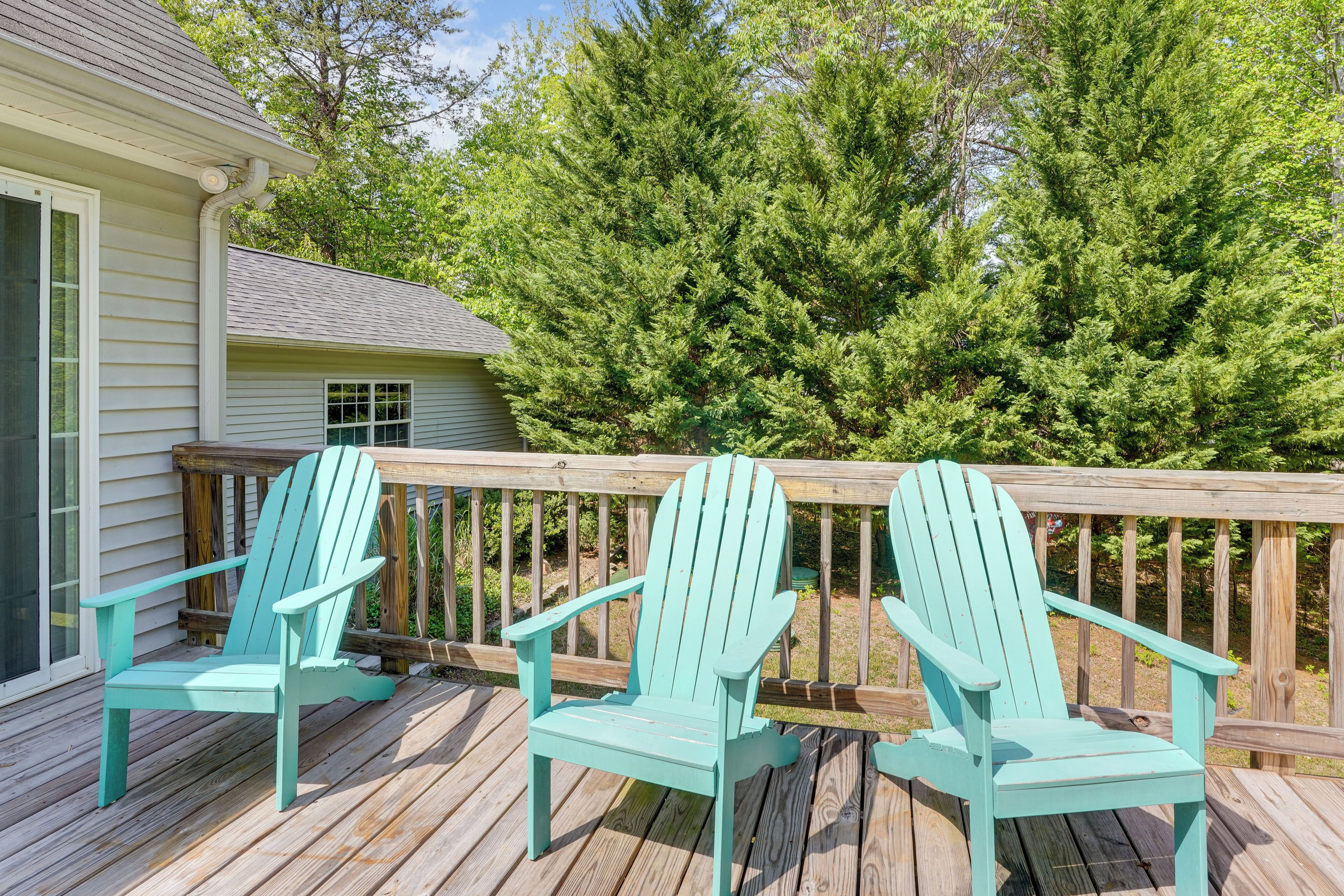 A wooden deck with two turquoise Adirondack chairs, a wooden railing, and a house with a window.