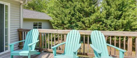 A wooden deck with two turquoise Adirondack chairs, a wooden railing, and a house with a window.