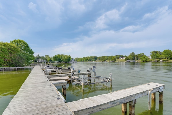 A wooden pier extending into a calm body of water with docked boats and a clear sky.
