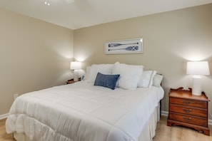 A bedroom with a large bed, two bedside tables with lamps, a wall-mounted artwork, and a wooden nightstand.