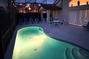 A swimming pool with a curved edge, surrounded by lounge chairs and a covered patio area. - Near Disney & Universal: Home w/ Pool & Spa! (Davenport)