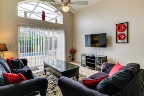 A living room with a sofa, a coffee table, a TV, and a decorative flower piece on the wall. - Near Disney & Universal: Home w/ Pool & Spa! (Davenport)