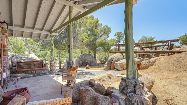 A covered outdoor area with a wooden bench, wicker chairs, and a stone table.