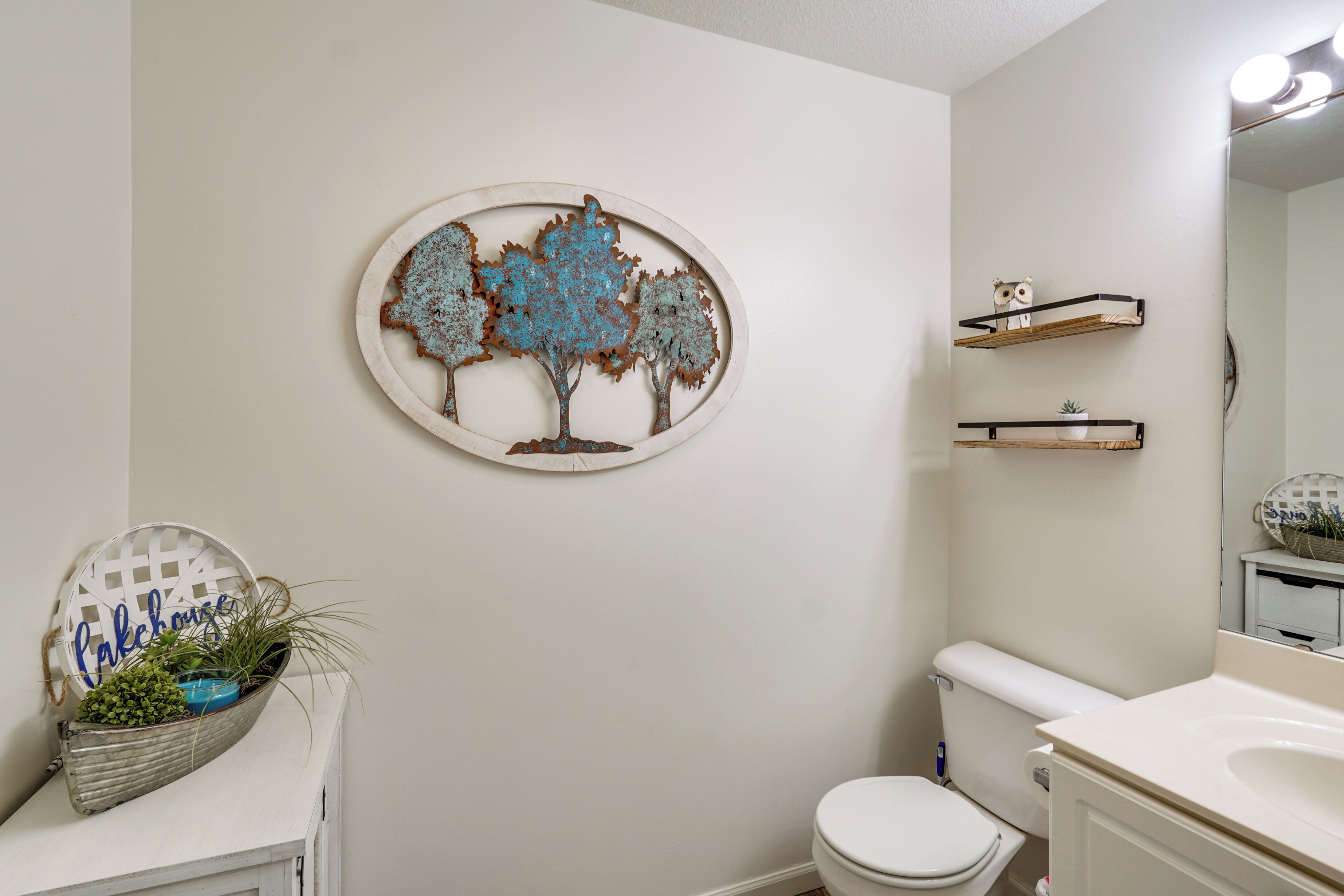 Een badkamer met toilet, wastafel, spiegel en decoratieve metalen wandkunst in de vorm van een boom.