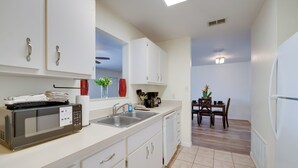 A modern kitchen with white cabinets, a microwave, sink, and a dining area with a table and chairs. - Steps to Crystal River! Dual-unit w/ Patios & Yard (Crystal River)