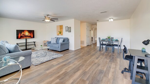 A modern living room with a sofa, TV, ceiling fan, and dining area with a table and chairs. - Steps to Crystal River! Dual-unit w/ Patios & Yard (Crystal River)