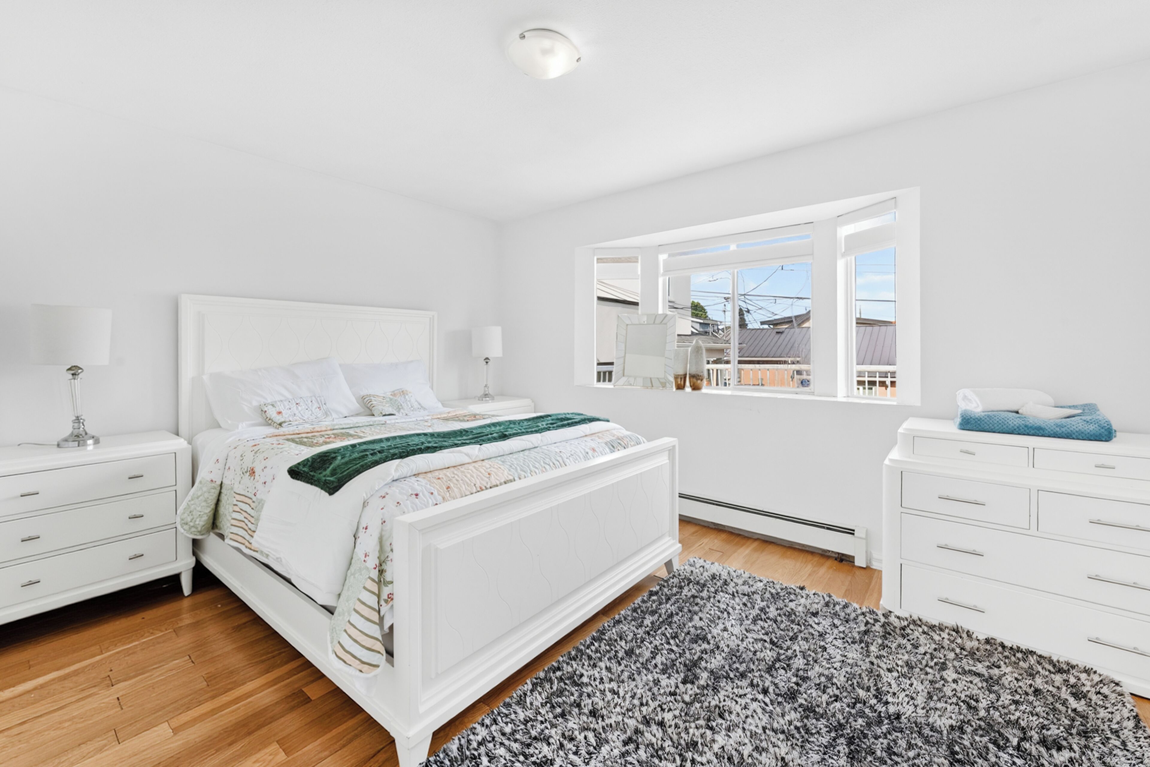 Une chambre à coucher comprenant un lit, des tables de chevet, une commode, une fenêtre avec vue et un luminaire au plafond.