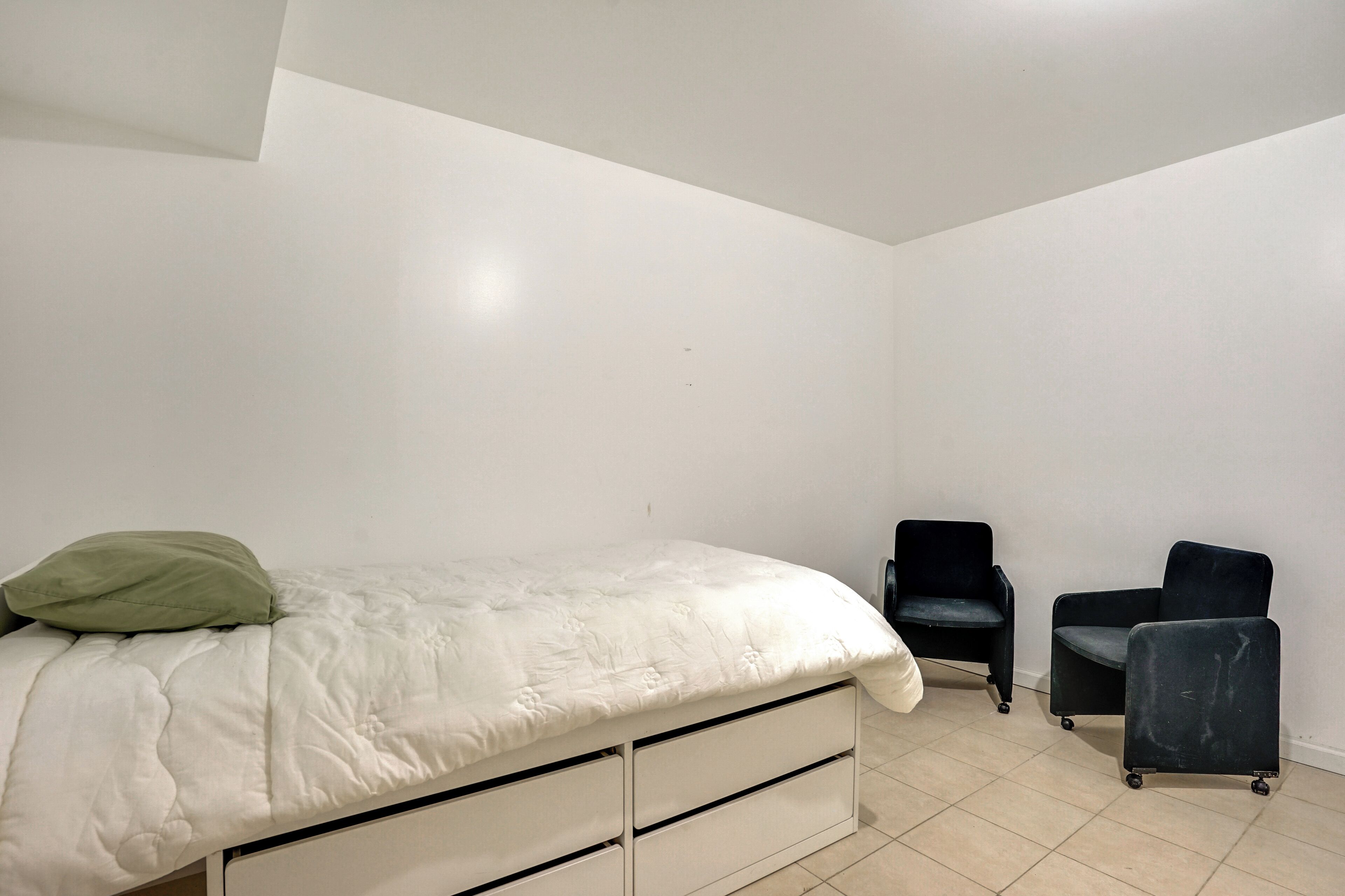 Ein Schlafzimmer mit einem Bett, zwei Stühlen und einer weißen Wand.