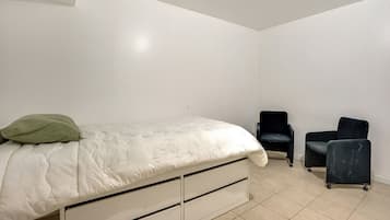 Ein Schlafzimmer mit einem Bett, zwei Stühlen und einer weißen Wand.