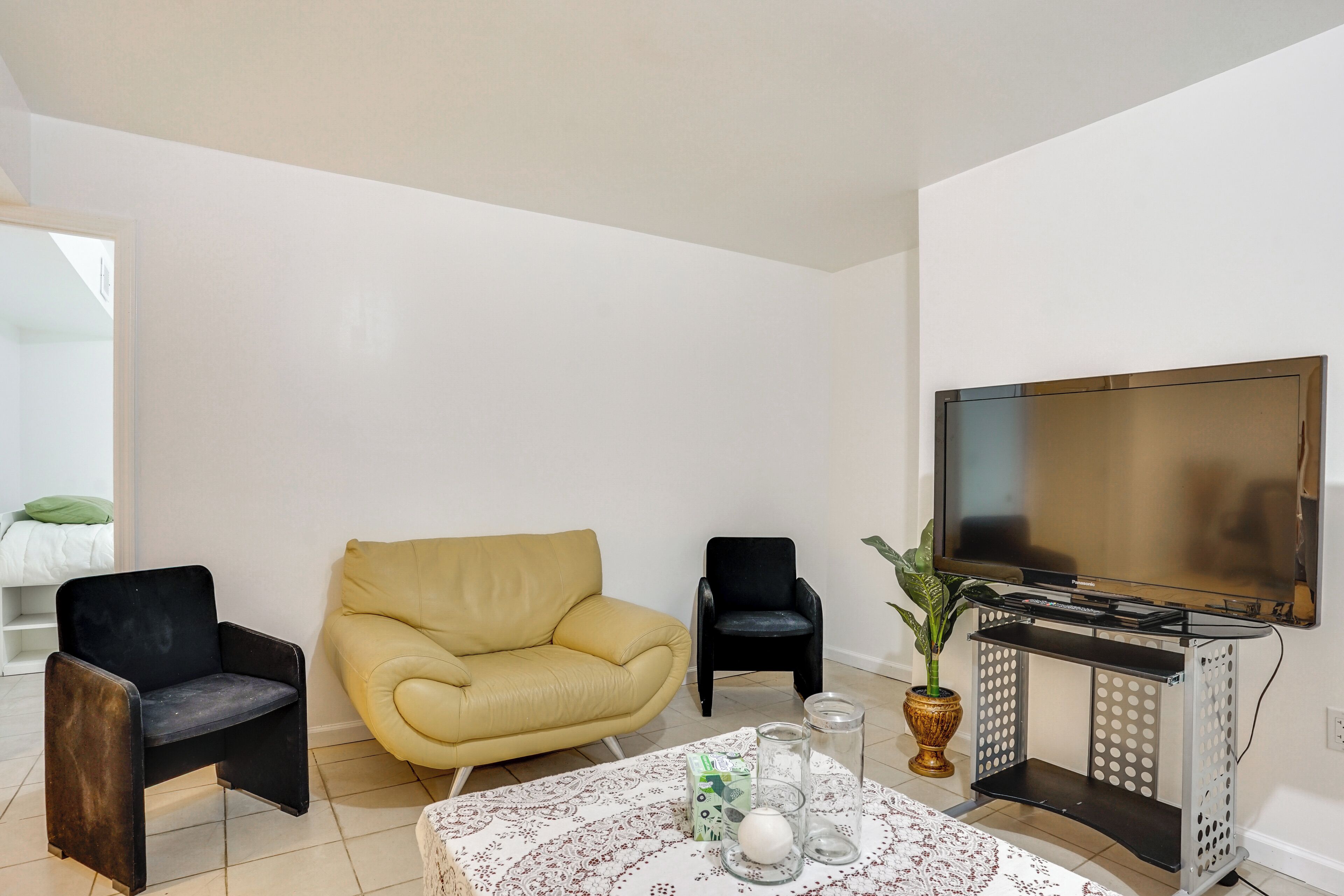 Un salon comprenant un canapé, deux fauteuils, une table basse agrémentée d’objets décoratifs, un téléviseur et une plante.