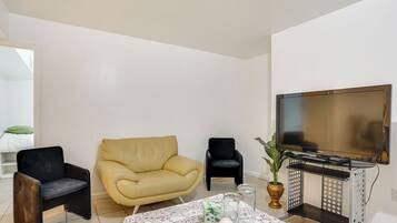 Un salon comprenant un canapé, deux fauteuils, une table basse agrémentée d’objets décoratifs, un téléviseur et une plante.