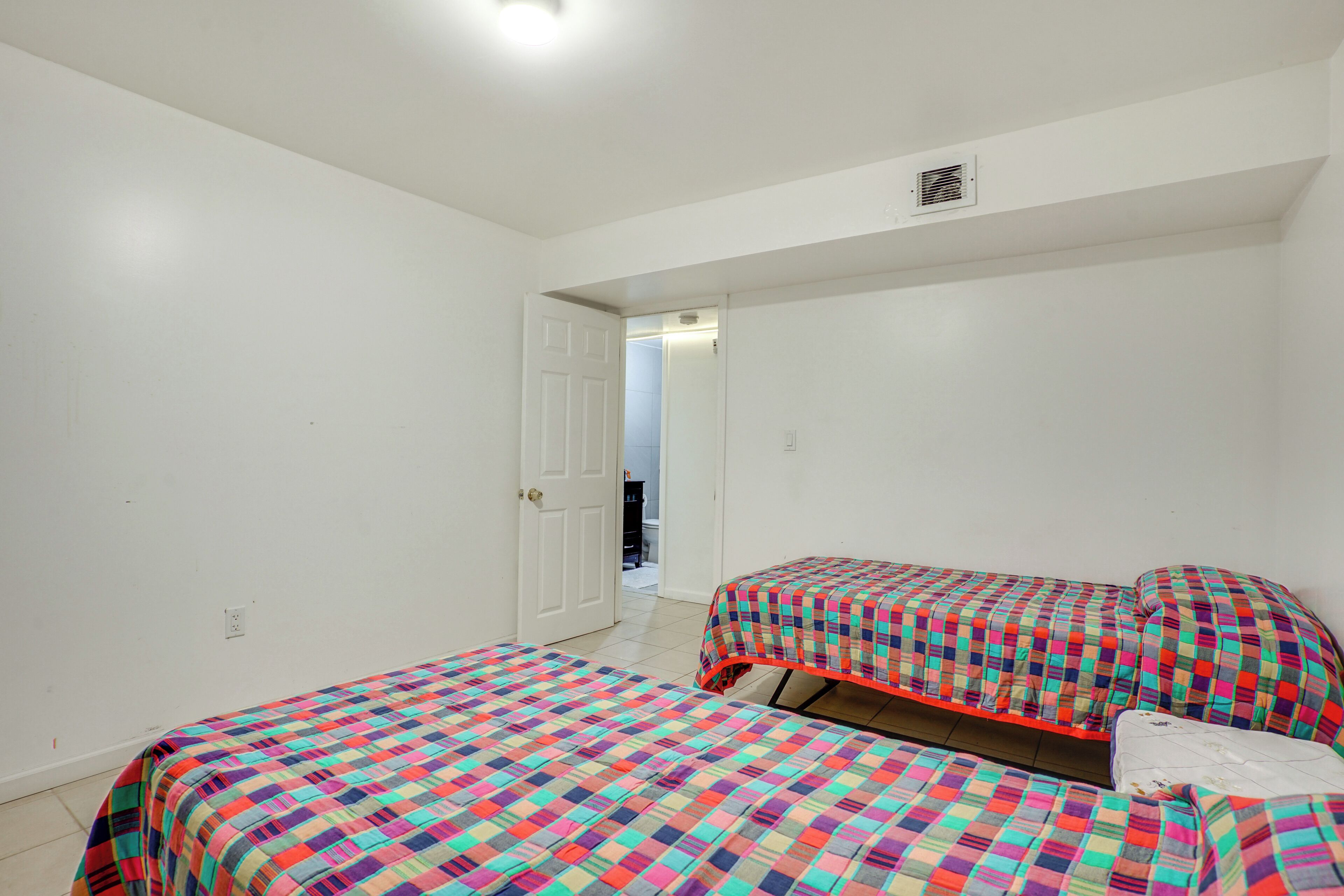 A bedroom with two beds, a white door, and a visible hallway.