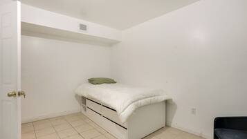 A bedroom with a bed, a door, a chair, and a wall socket.