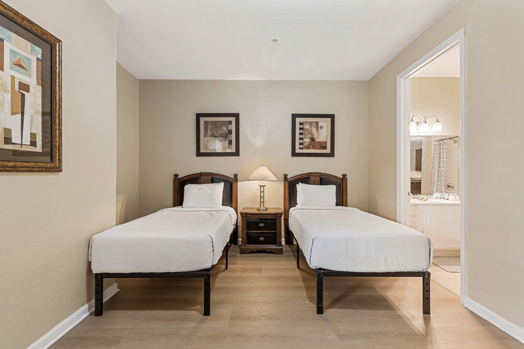 A hotel room with two single beds, a nightstand with a lamp, and a framed picture on the wall.