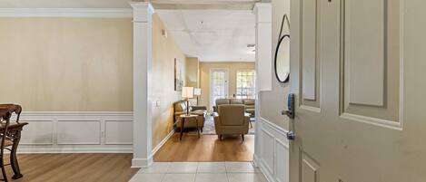 A hallway with a dining area, a living room with a sofa and armchairs, and a door with a security device.