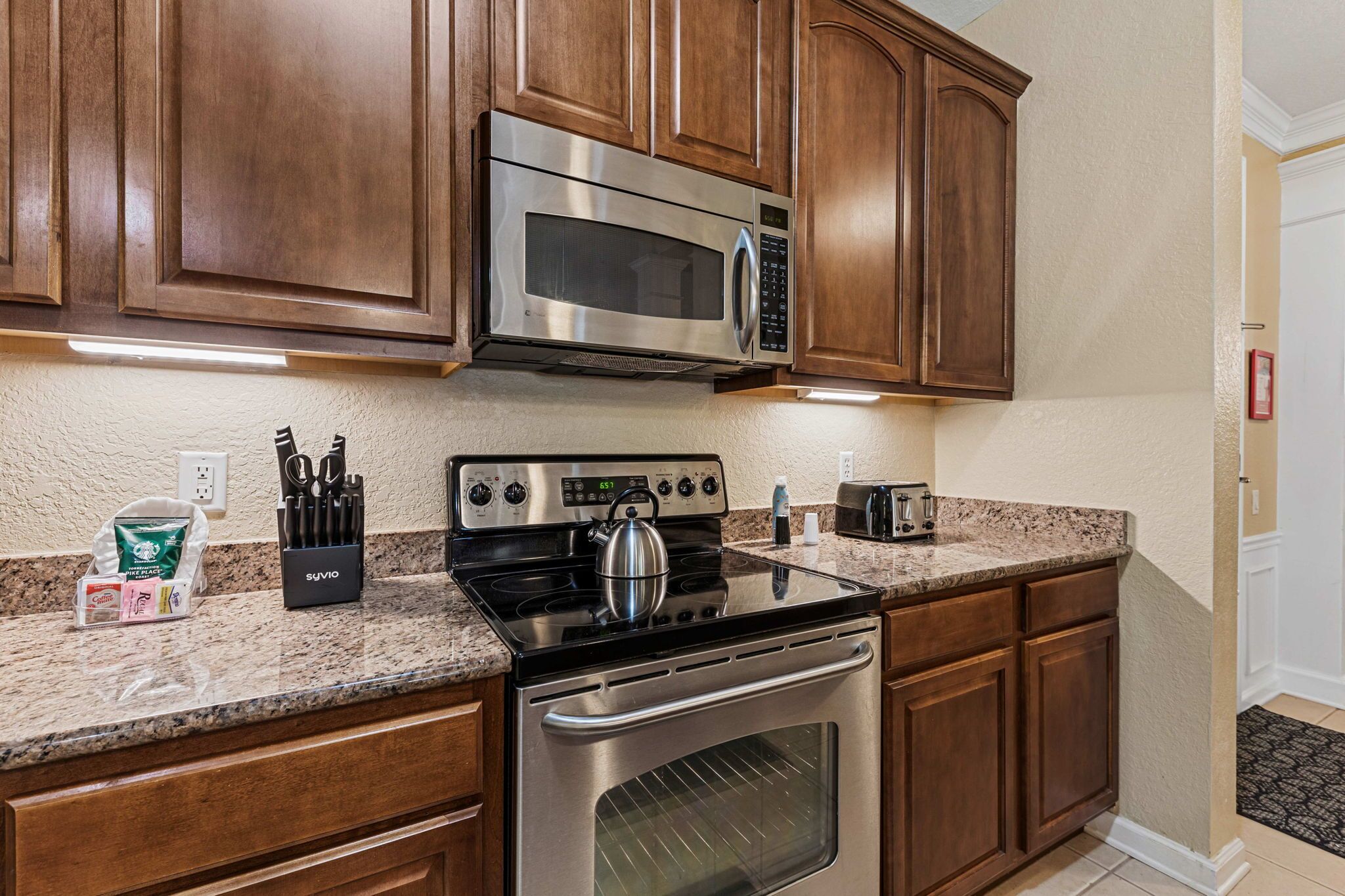A kitchen with wooden cabinets, a stainless steel microwave, a stove, and a toaster.