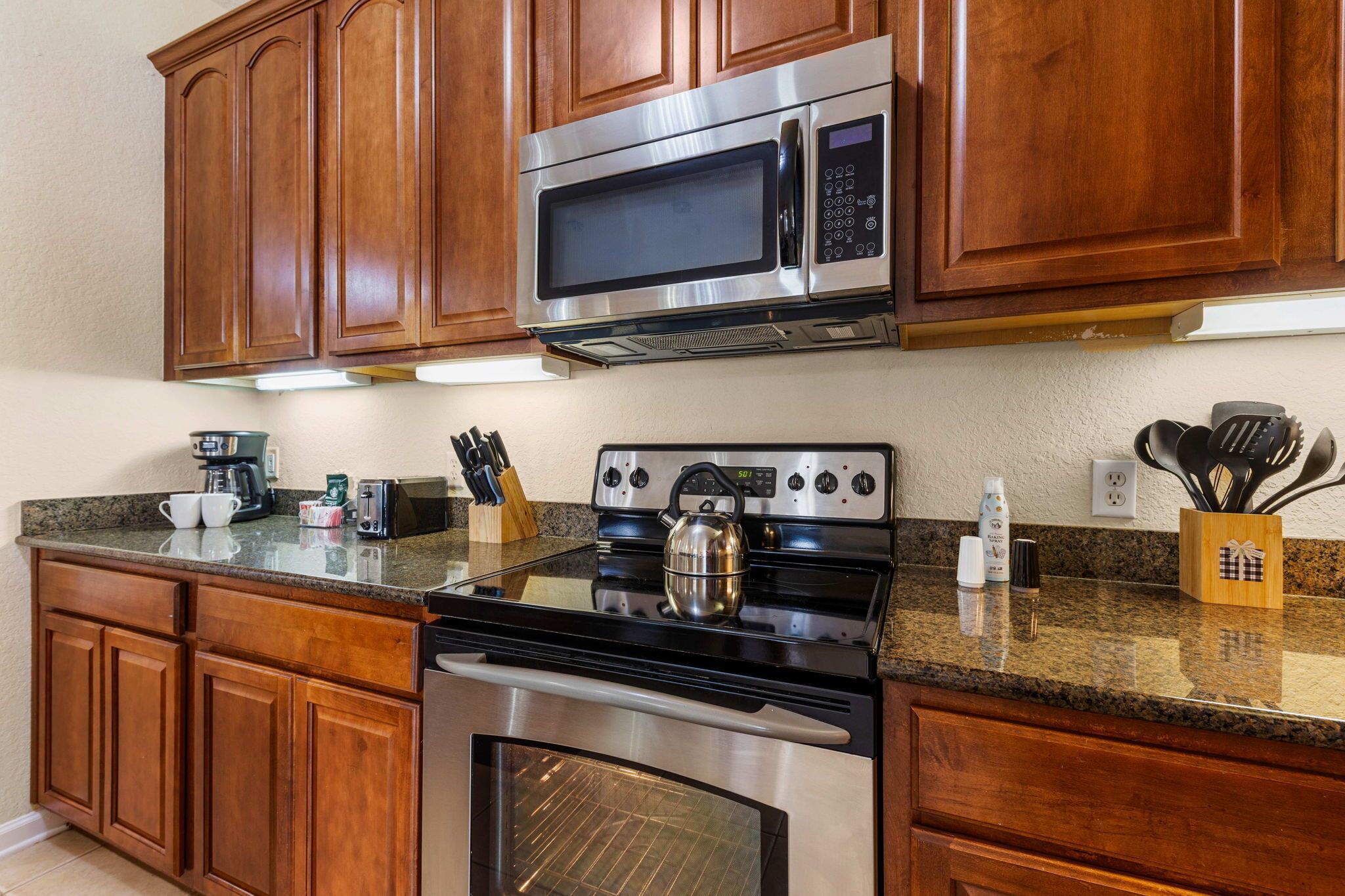 A kitchen with wooden cabinets, stainless steel appliances, granite countertops, and various kitchen utensils.