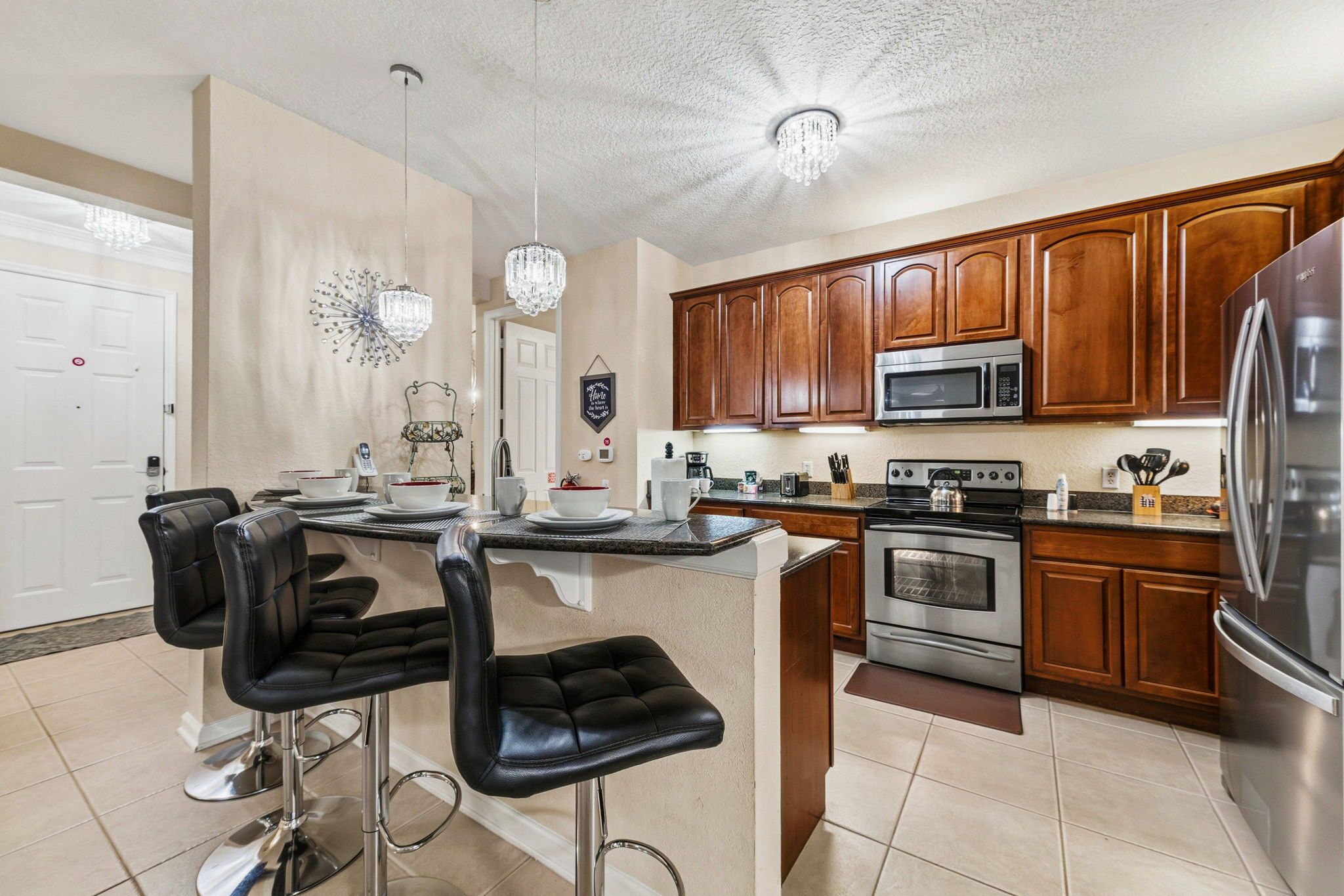A kitchen with wooden cabinets, stainless steel appliances, a bar area with stools, and pendant lighting.
