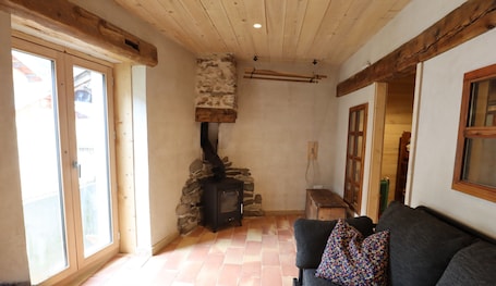 A room with a stone fireplace, a wooden ceiling, a couch, and a window.