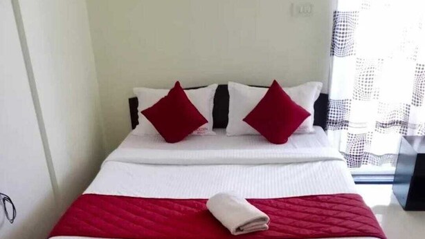 Una cama con estructura negra, ropa de cama blanca y detalles en rojo.