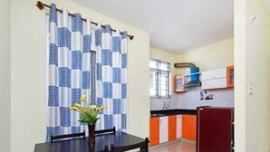 Una cocina compacta con comedor, un refrigerador rojo y una ventana con cortinas.