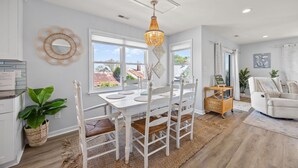 A dining area with a white table and chairs, a chandelier, and a view of the outside. - Bay Watch w/Elevator (Pet Friendly Home) (Morehead City)