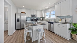 A modern kitchen with white cabinets, stainless steel appliances, a granite countertop, and a bar area with stools. - Bay Watch w/Elevator (Pet Friendly Home) (Morehead City)