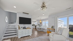 A modern living room with a flat-screen TV, a ceiling fan, a dining area, and a view of the sea. - Bay Watch w/Elevator (Pet Friendly Home) (Morehead City)