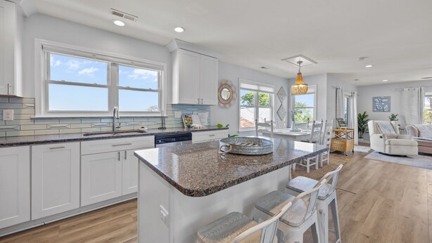 A modern kitchen with white cabinets, granite countertops, and a large island with bar stools. - Bay Watch w/Elevator (Pet Friendly Home) (Morehead City)