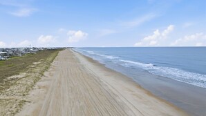 Een lang, zandstrand met een helder uitzicht op de oceaan en een rij huizen op de achtergrond.