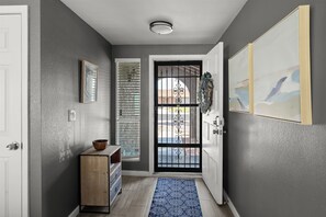 A hallway with a door, a window with blinds, a small wooden cabinet, a blue patterned rug, and a wall-mounted artwork. - Private Heated Pool Perfect for Groups (Peoria)