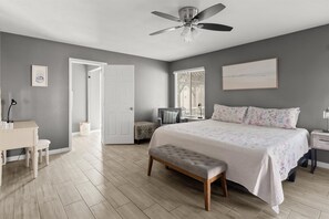 A bedroom with a bed, a desk, a chair, a bench, a ceiling fan, a window, and a door. - Private Heated Pool Perfect for Groups (Peoria)