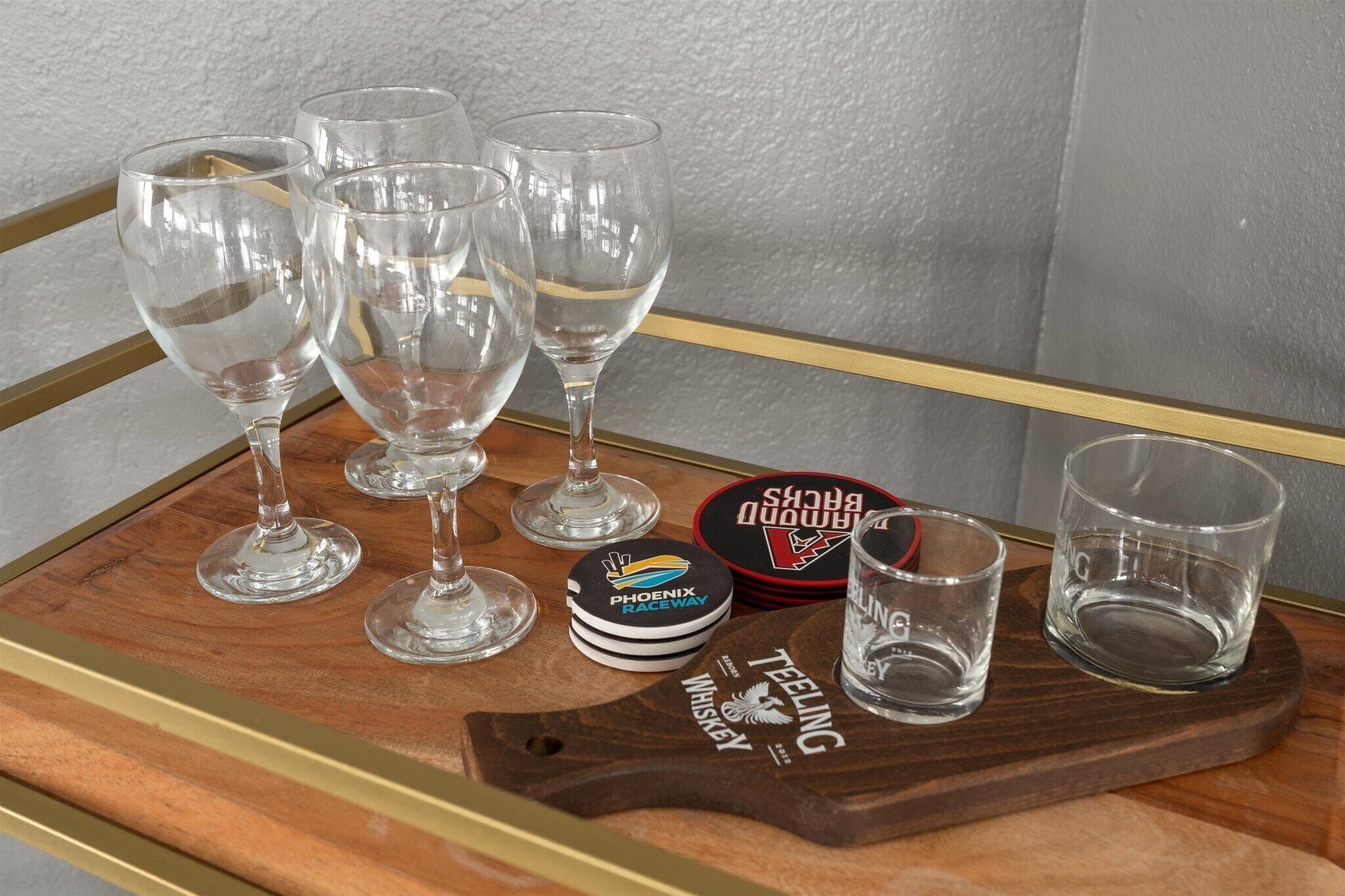 A tray with wine glasses, a whiskey tin, and coasters on a wooden table.