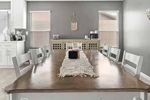 A dining area with a long wooden table, white chairs, a macrame runner, and a dreamcatcher on the wall. - Private Heated Pool Perfect for Groups (Peoria)