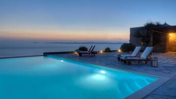 A swimming pool with lounge chairs and a stone building with a light.